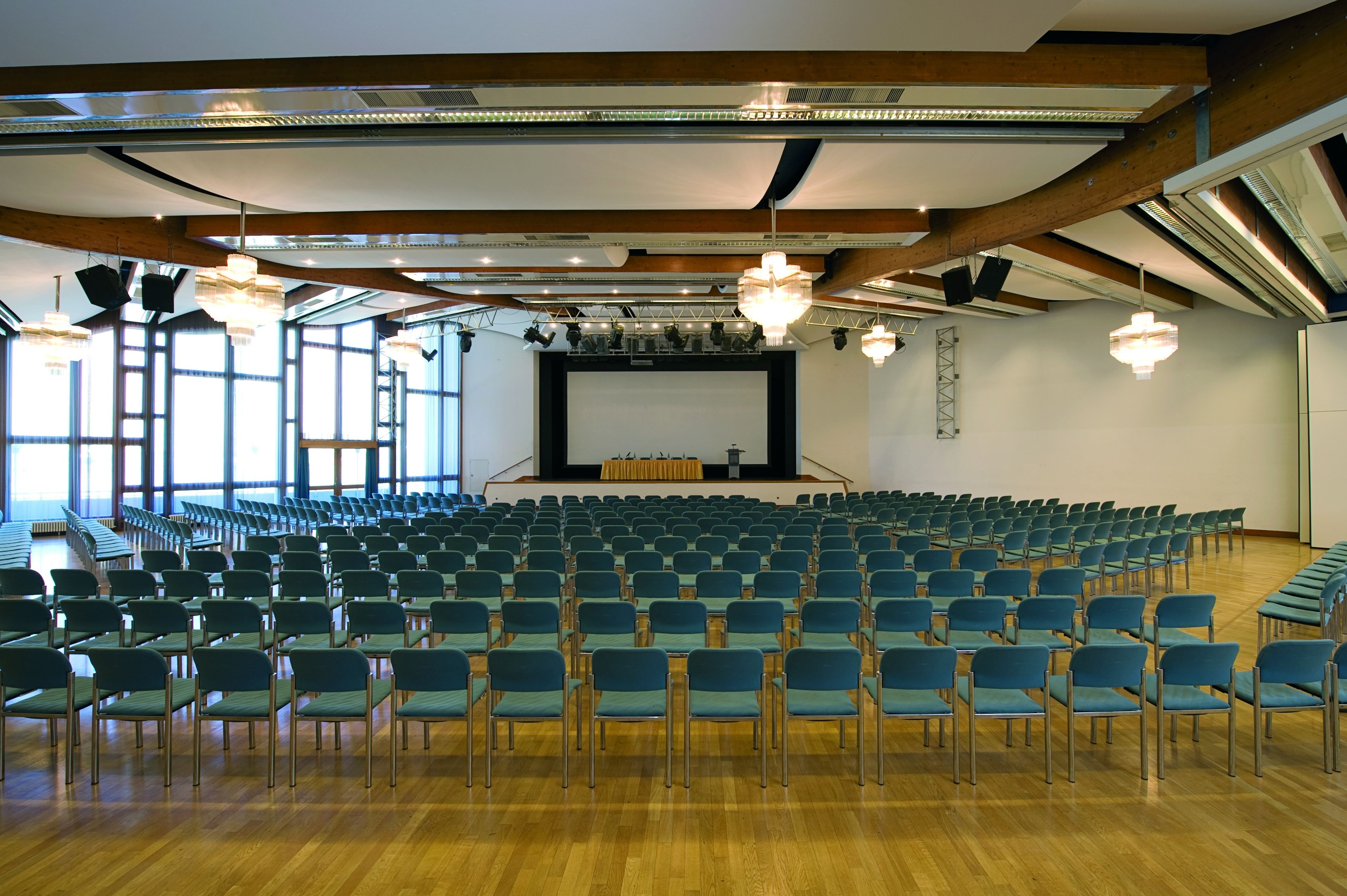 Une grande salle avec des rangées de chaises, une scène dotée d’un pupitre et de grandes fenêtres.