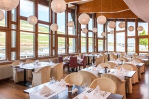 A restaurant with large windows, wooden beams, and hanging paper lanterns. Tables are set with white tablecloths and wine glasses.