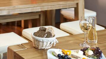 Una mesa de madera con un plato de queso, uvas y pan, una copa de vino blanco y una vela.