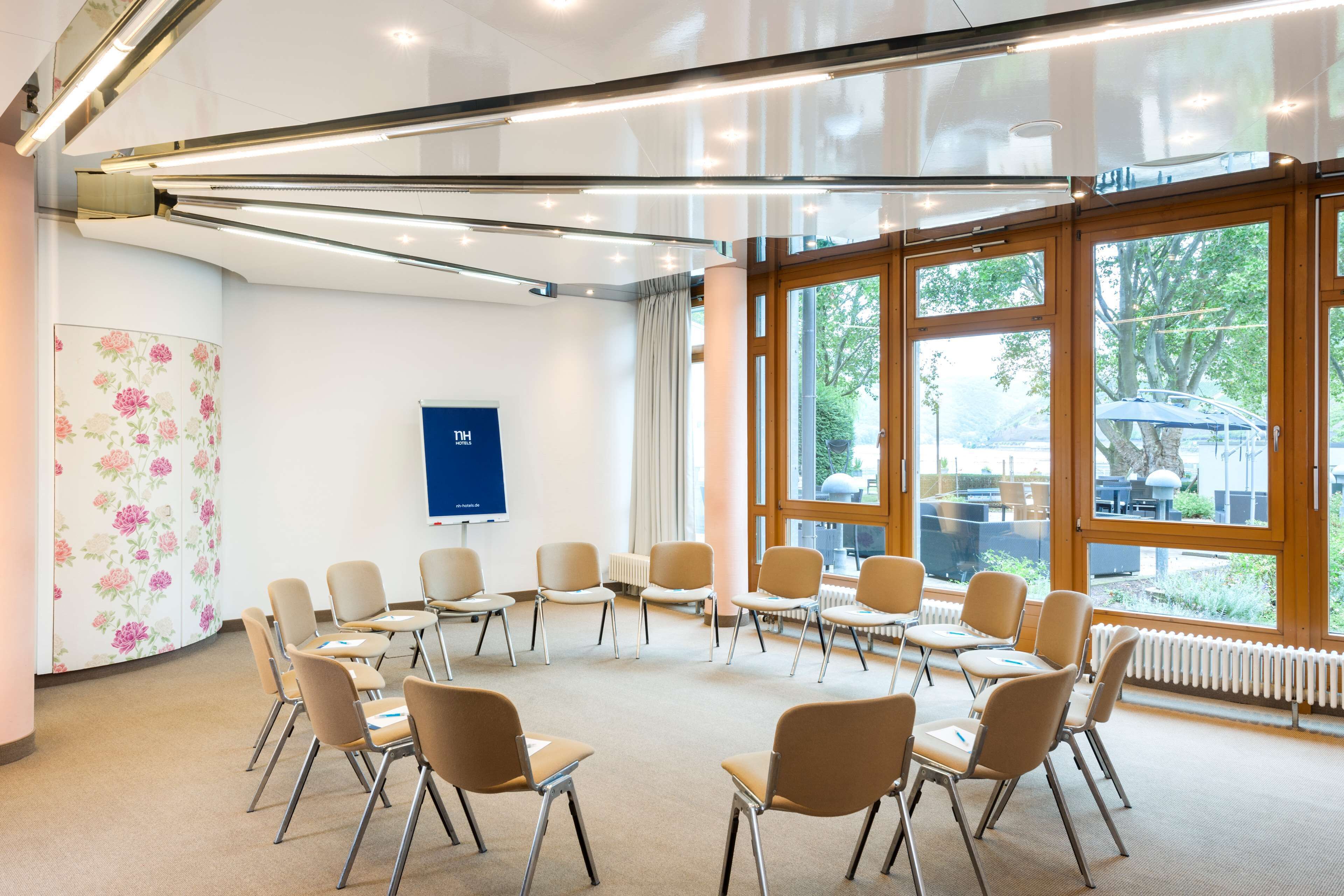 A conference room with a circular arrangement of chairs, large windows, and a visible blue sign on the wall.