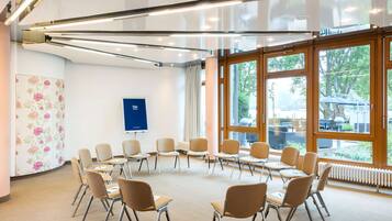 A conference room with a circular arrangement of chairs, large windows, and a visible blue sign on the wall.