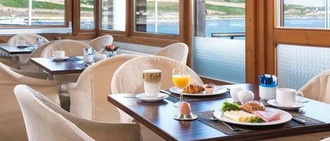 A breakfast setting with a table, chairs, and a view of the sea.