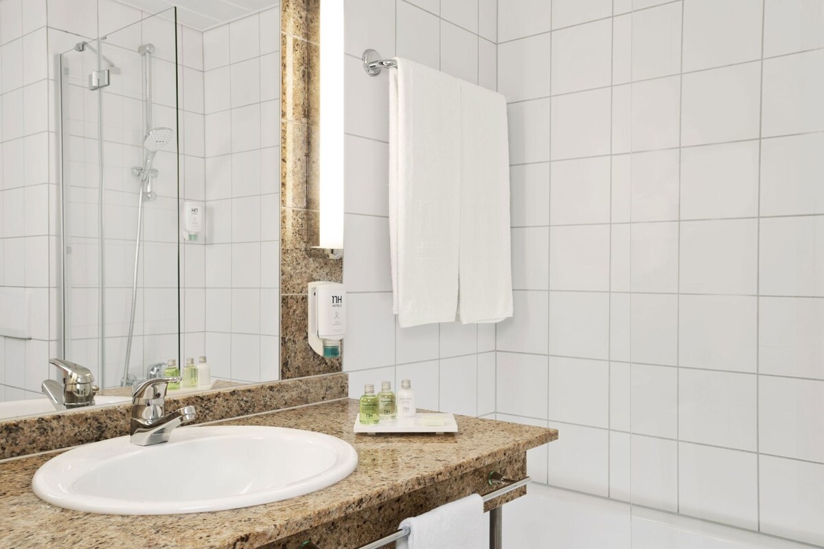 Uma casa de banho moderna com bancada de granito, lavatório branco, chuveiro manual, porta-toalhas e espelho.