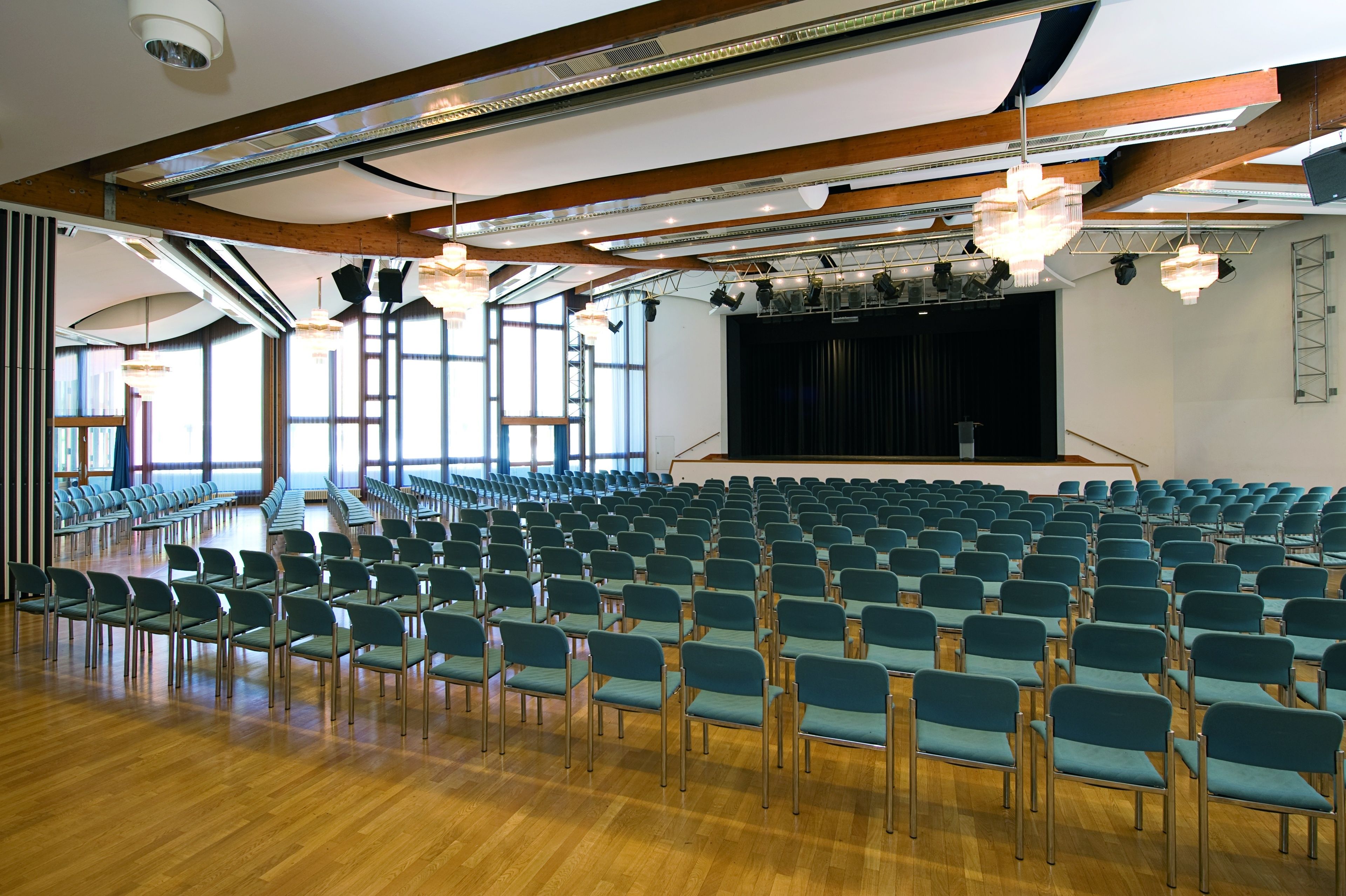 Un ampio auditorium con file di sedie verdi, travi di legno a soffitto e un palcoscenico con uno sfondo nero.