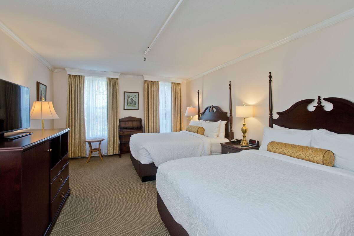 A hotel room with two beds, a TV, a desk, and a chair.