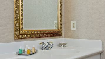 A bathroom with a white sink, gold-framed mirror, and toiletries on the counter.