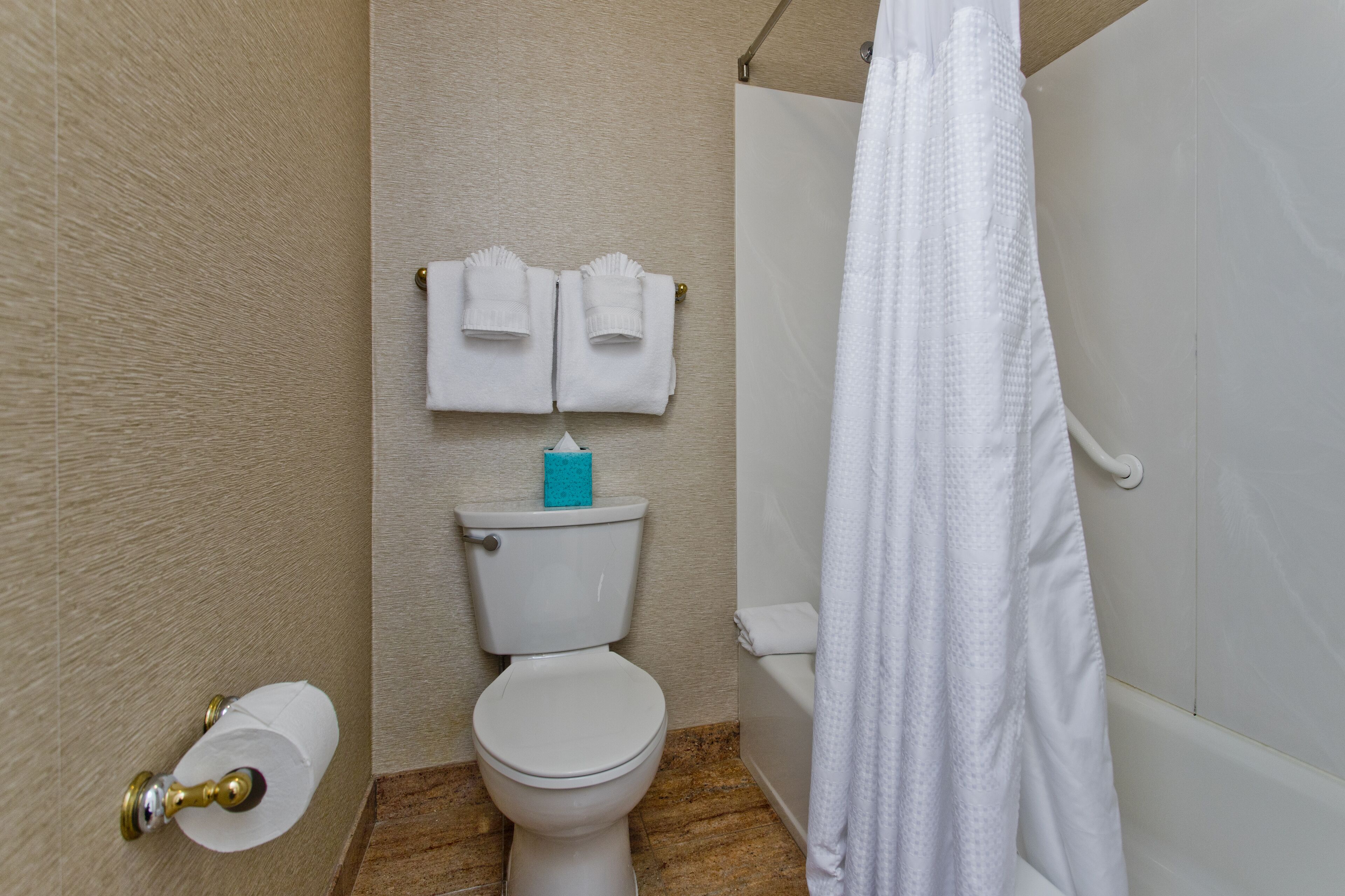 A bathroom with a toilet, a shower curtain, and two towels hanging on the wall.