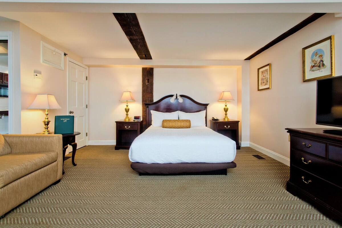 A hotel room with a large bed, two bedside tables with lamps, a dresser, a television, and a framed picture on the wall.