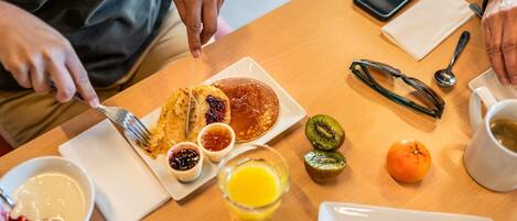 A breakfast setting with pancakes, fruit, and croissants on a wooden table.