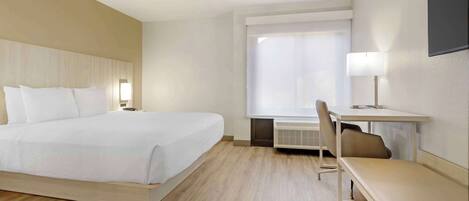 Una habitación de hotel con una cama, un escritorio, una silla, un banco y un ventanal grande.