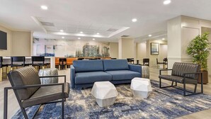 A modern lounge area with a blue sofa, two leather chairs, and a geometric rug. - Best Western Plus Sugar Land/Stafford (Sugar Land)