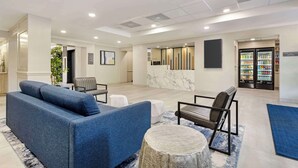A spacious lobby with a blue sofa, a marble reception desk, and a refrigerator stocked with beverages. - Best Western Plus Sugar Land/Stafford (Sugar Land)