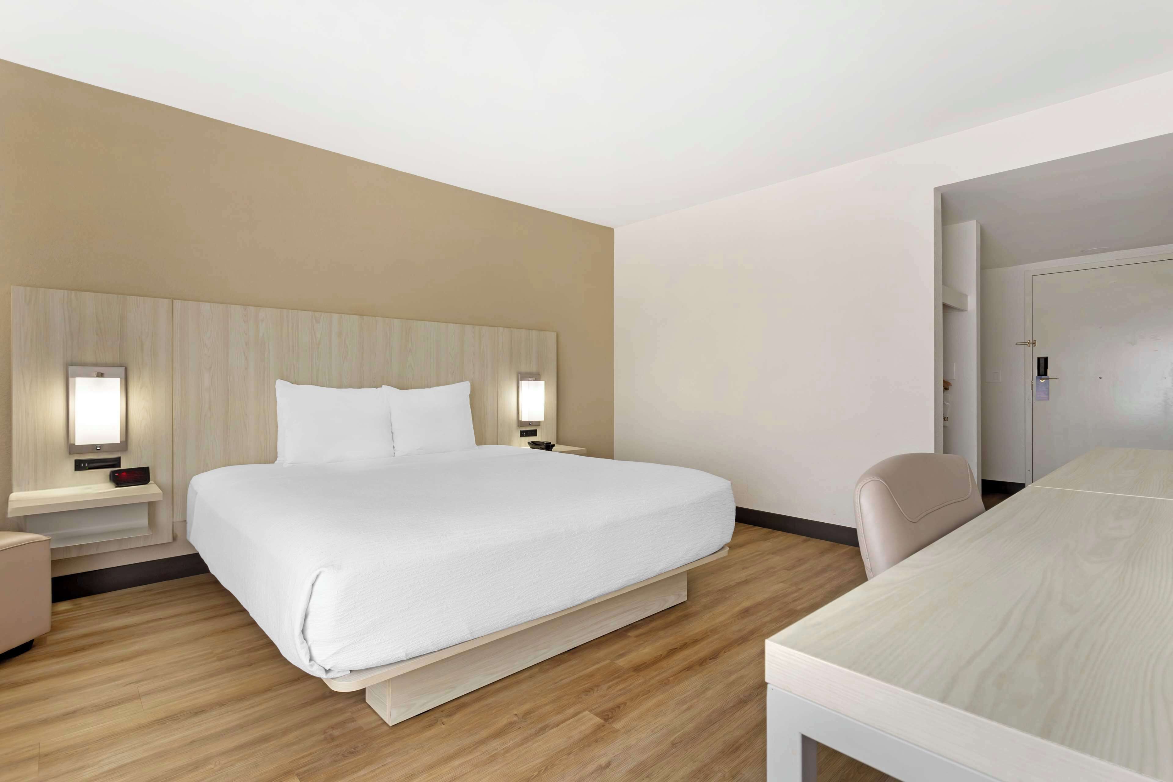 A hotel room with a large bed, bedside tables, a chair, and a desk.