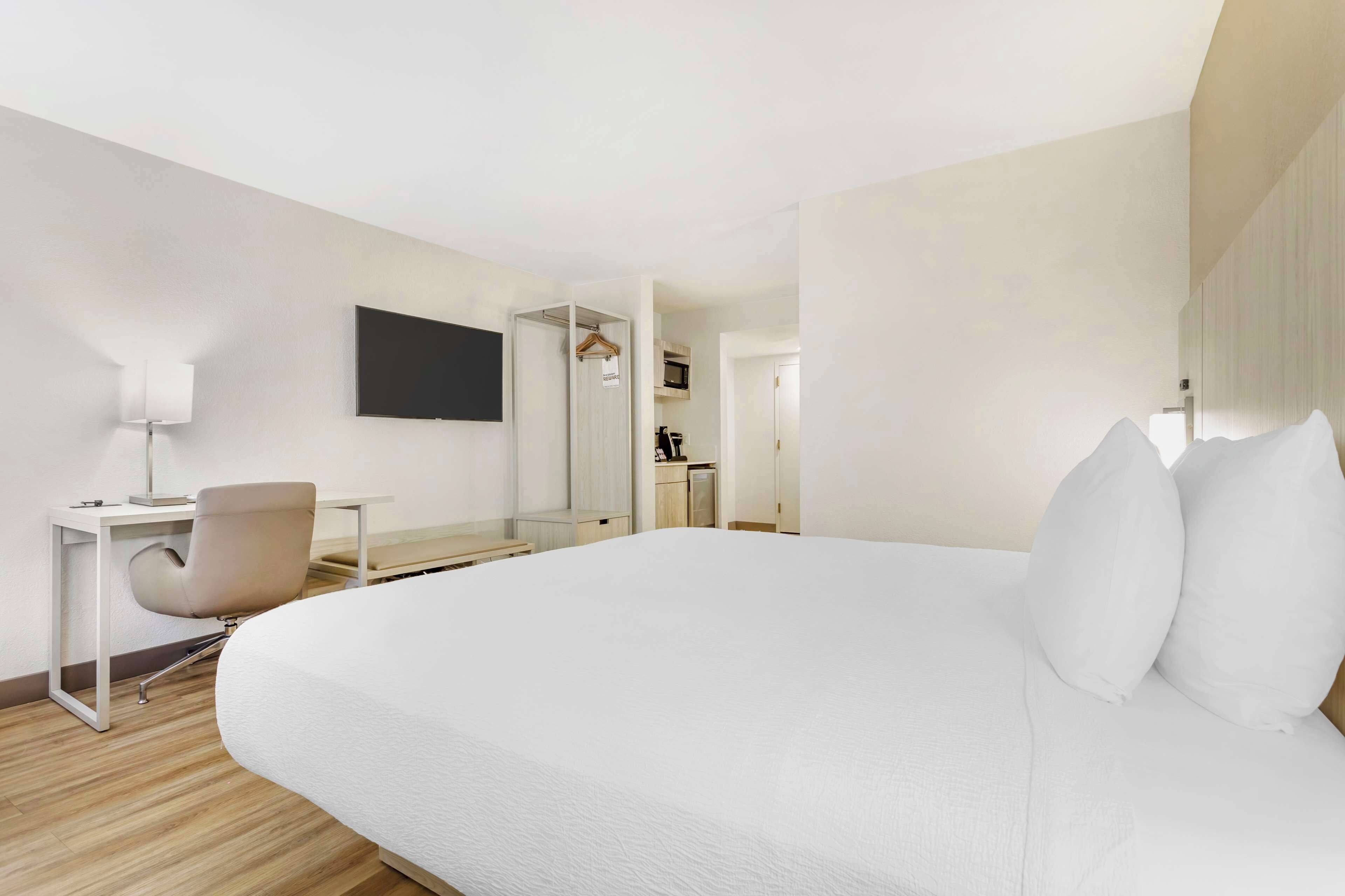 A modern hotel room with a large bed, a desk with a chair, a flat-screen TV, and a walk-in closet.