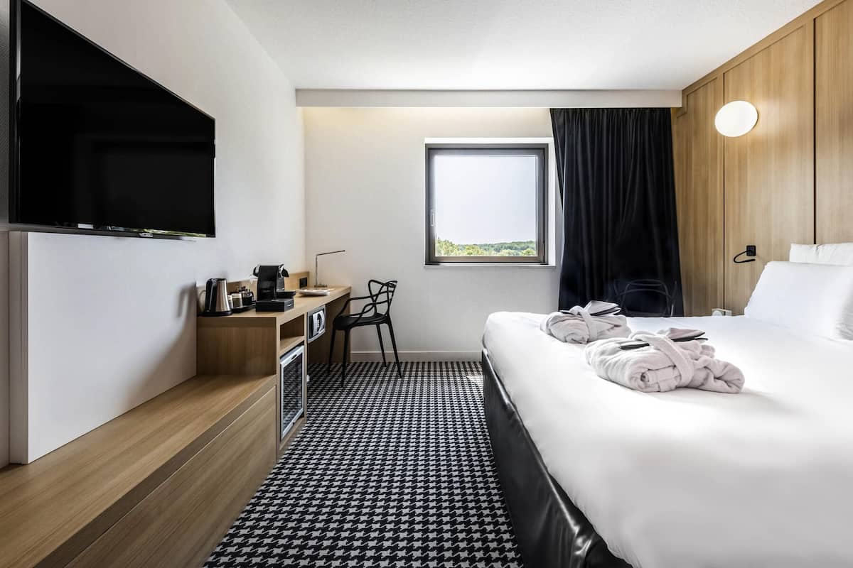 A hotel room with a bed, a desk, a TV, a window with a view, and a bathroom.