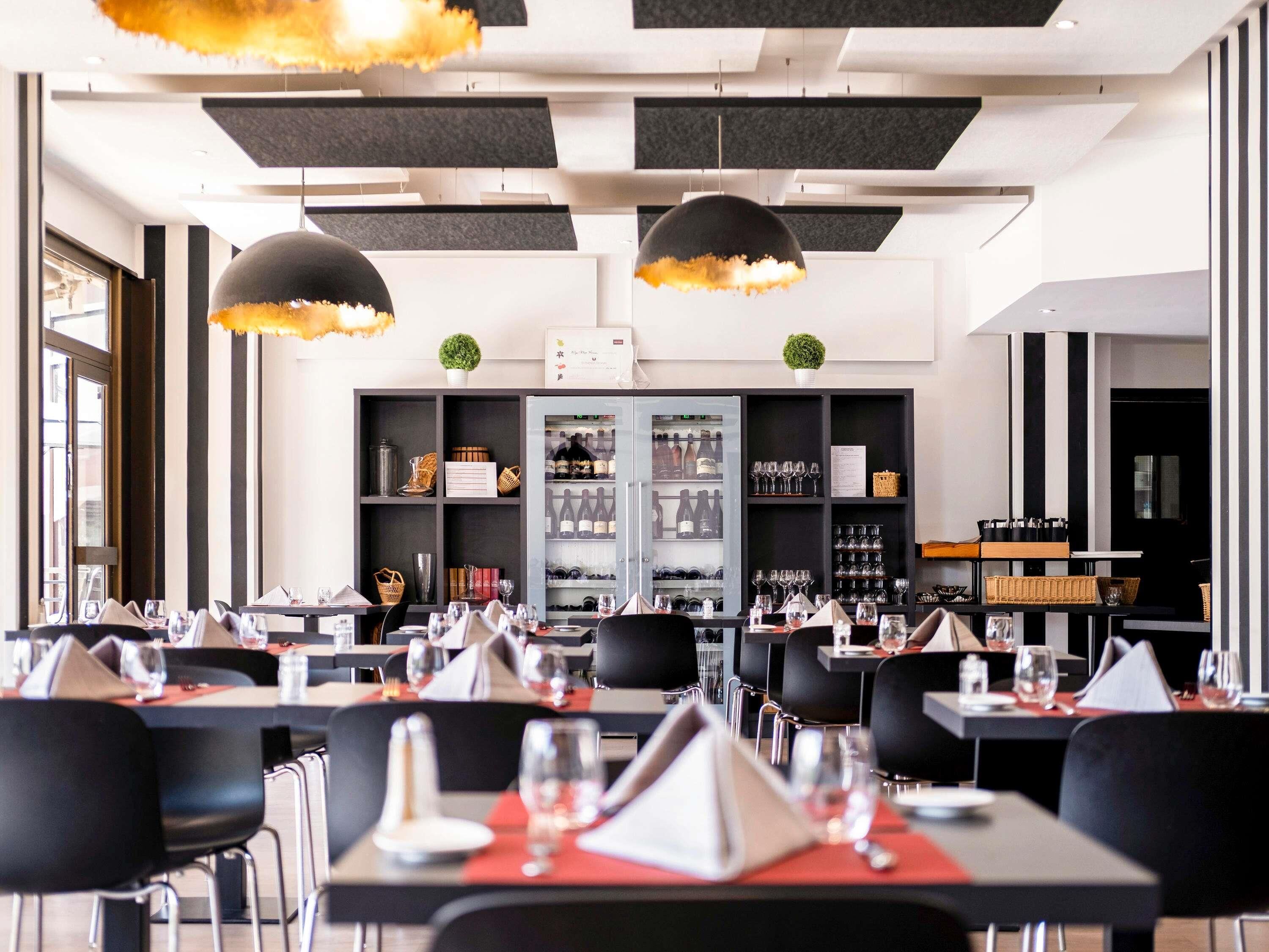 Interior moderno de restaurante con decoración blanco y negro, varias mesas de comedor y lámparas colgantes.
