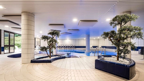 Ein moderner Innenpoolbereich mit Fliesenboden, Sitzgelegenheiten am Pool und Kübelpflanzen.