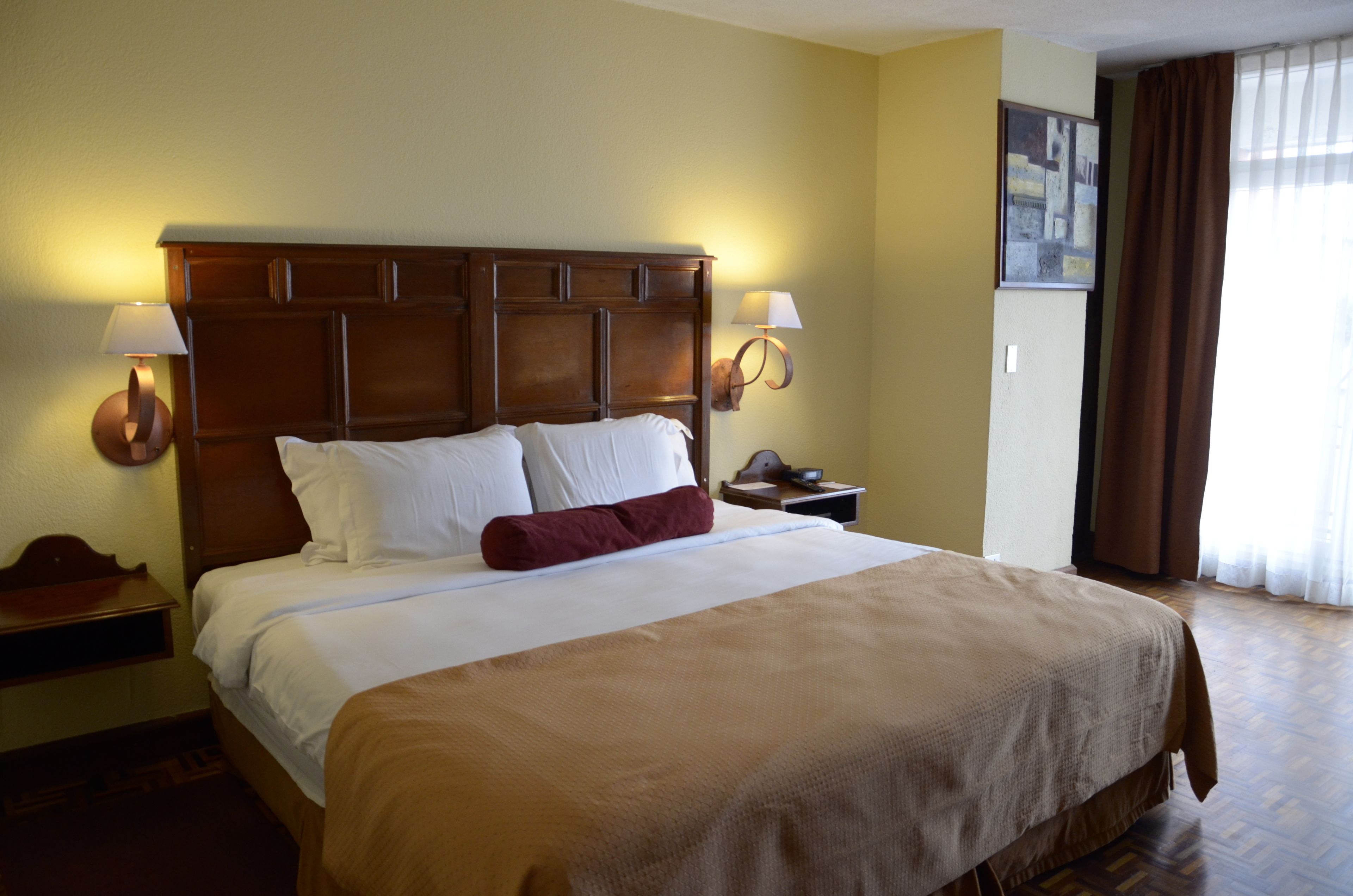 A hotel room with a large bed, two bedside lamps, a nightstand, and a painting on the wall.