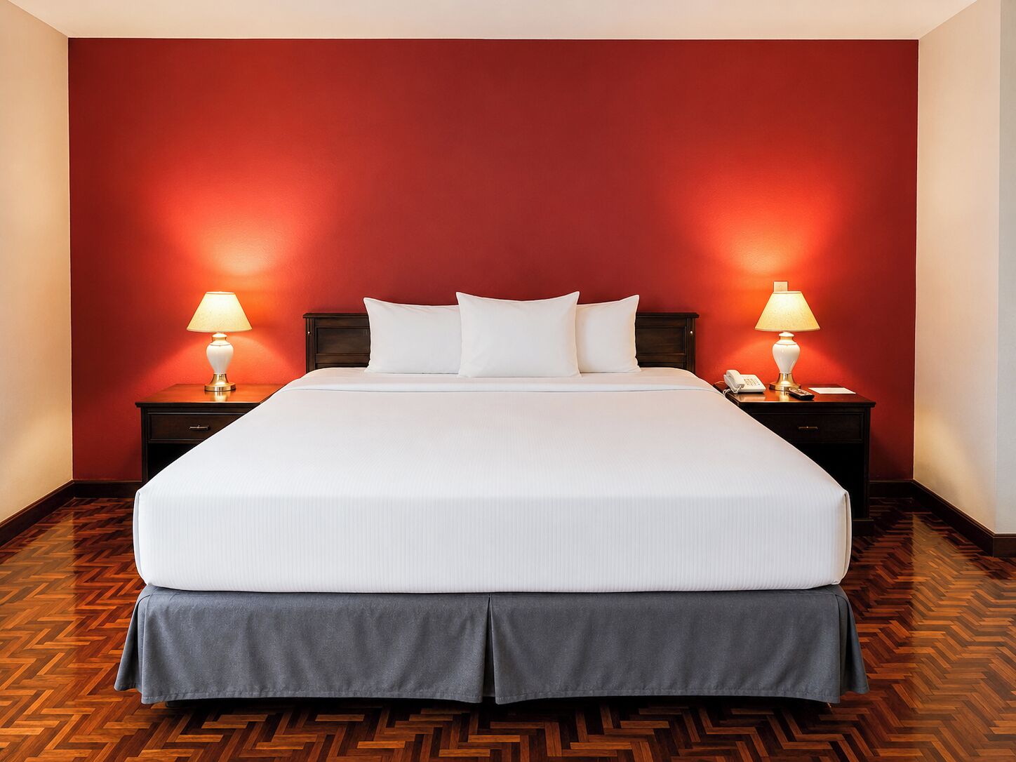 Quarto de hotel com uma cama grande, duas mesas de cabeceira com luminárias, um telefone e um piso de madeira com padrão herringbone.