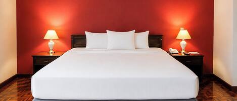 Quarto de hotel com uma cama grande, duas mesas de cabeceira com luminárias, um telefone e um piso de madeira com padrão herringbone.