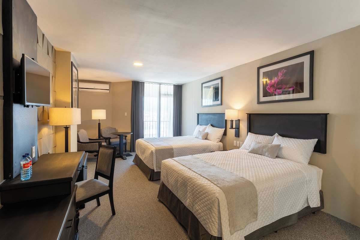 A hotel room with two beds, a desk, a chair, a TV, and a framed picture on the wall.