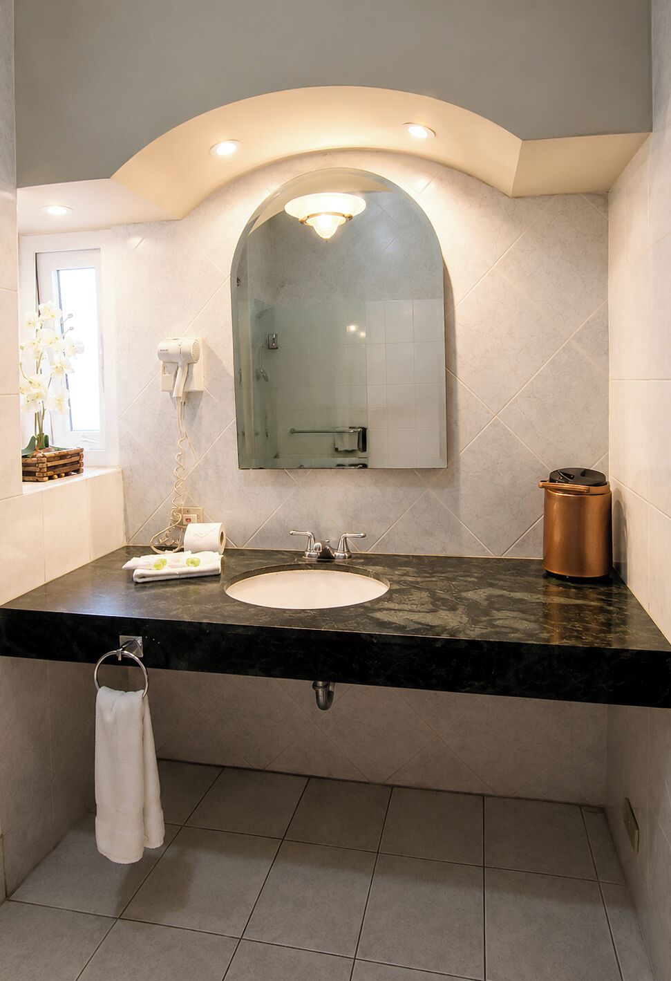 Uma casa de banho com lavatório, espelho, porta-toalhas e secador de cabelo na parede.