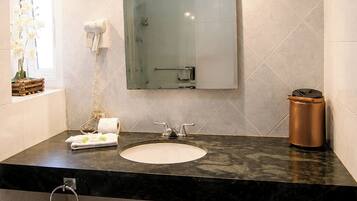 Uma casa de banho com lavatório, espelho, porta-toalhas e secador de cabelo na parede.