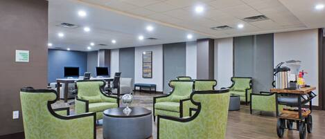 A spacious lobby with green patterned chairs, a round coffee table, and a reception desk.
