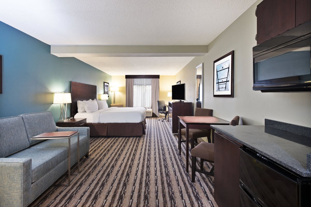 A hotel room with a bed, a sofa, a desk, a television, and a flat-screen TV mounted on the wall.