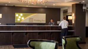 Un comptoir d'accueil d'un hôtel Holiday Inn, agrémenté d'un lustre moderne, d'un écran numérique et doté d'un intérieur épuré aux couleurs sombres.