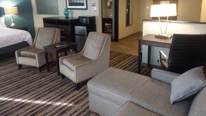 Une chambre d’hôtel comprenant un lit, deux fauteuils, un canapé, un bureau avec une lampe, une télévision et un four à micro-ondes.