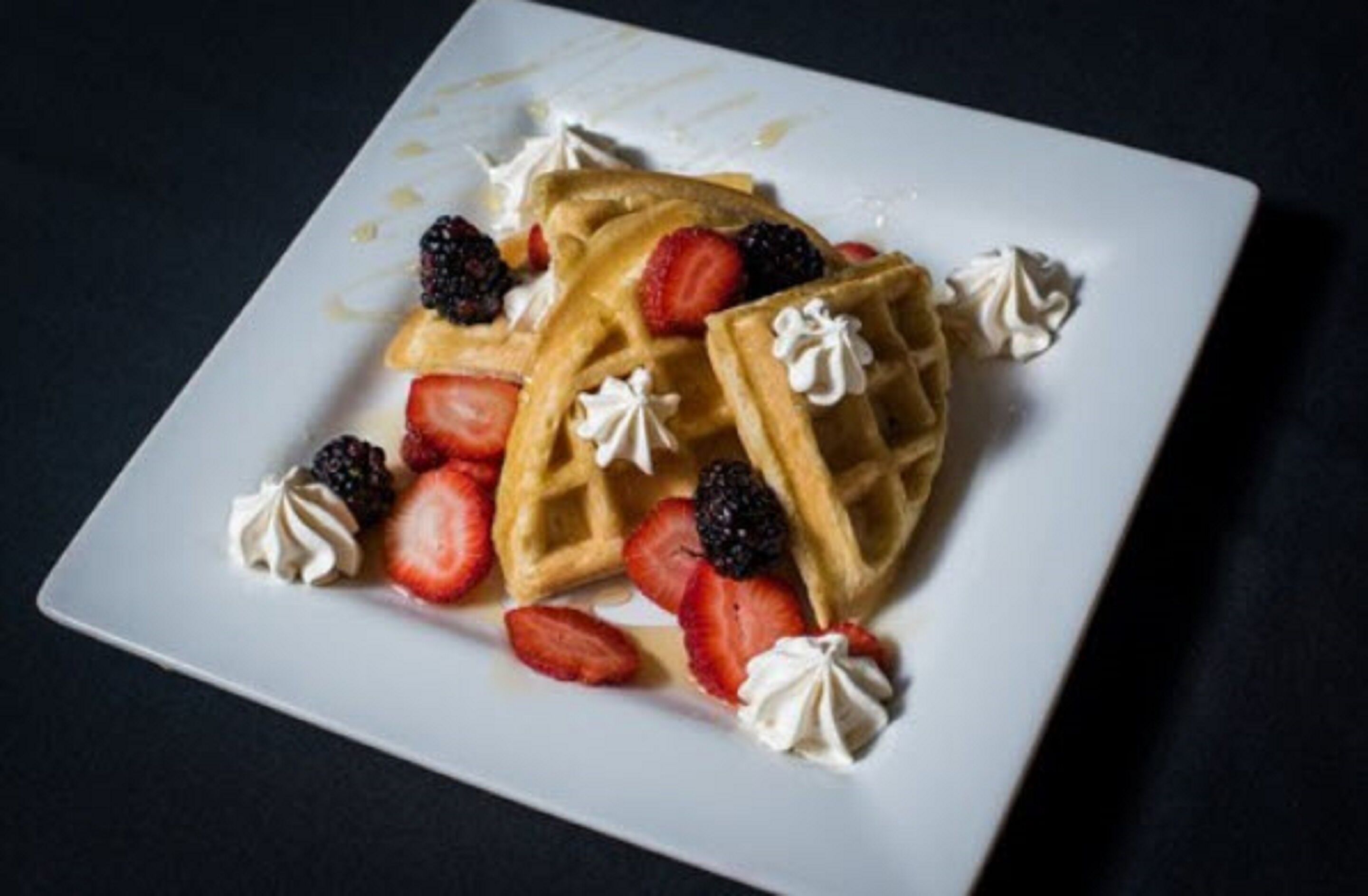 Un plato cuadrado con gofres cubiertos de fresas, zarzamoras y crema batida.