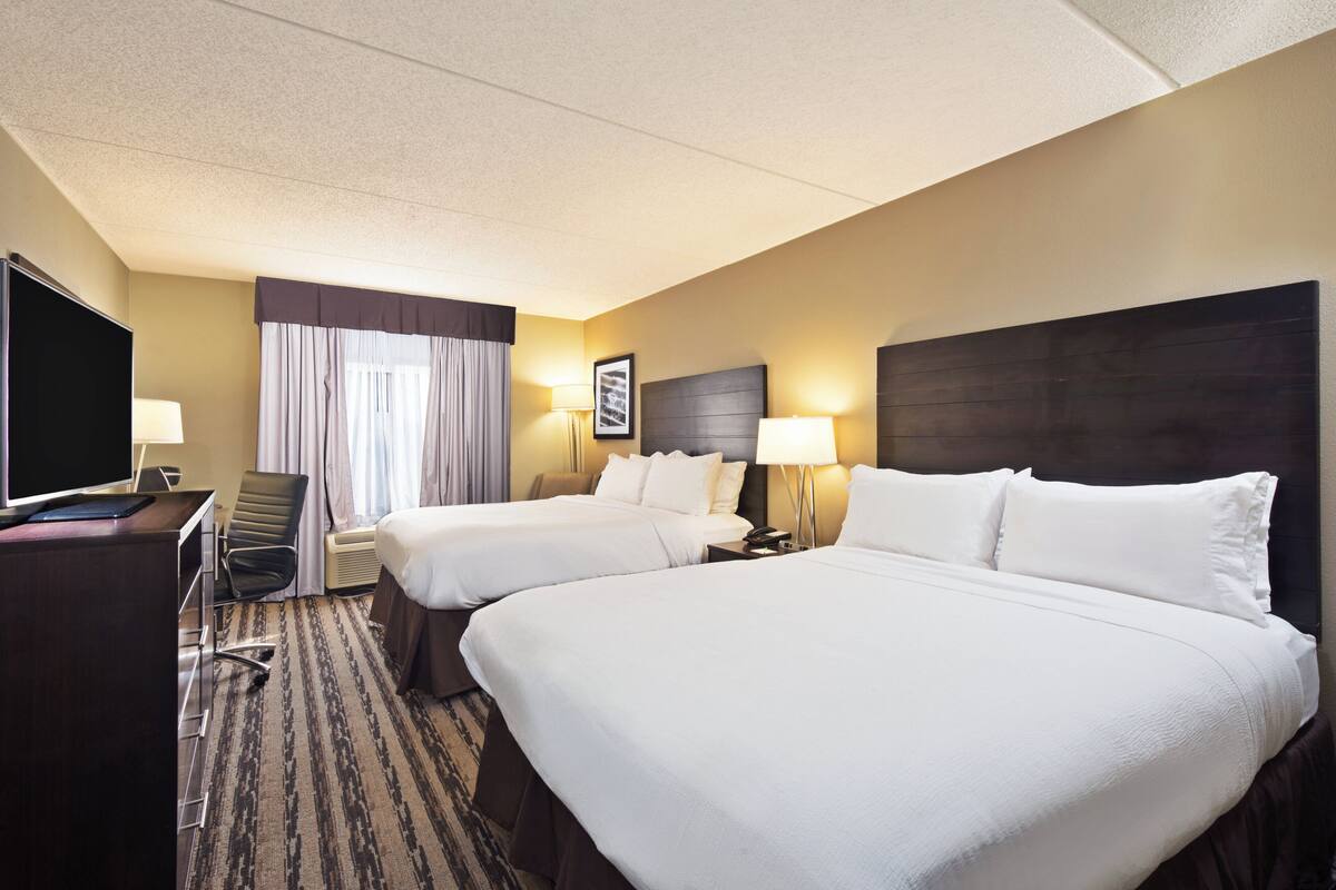 A hotel room with two beds, a desk with a flat-screen TV, a chair, a lamp, and a framed picture on the wall.