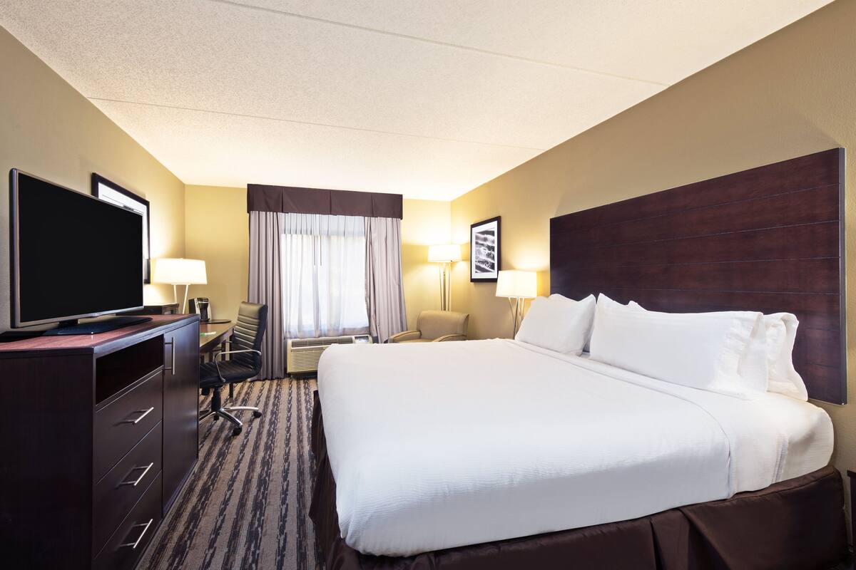 A hotel room with a large bed, a desk with a computer, a TV, and a chair.