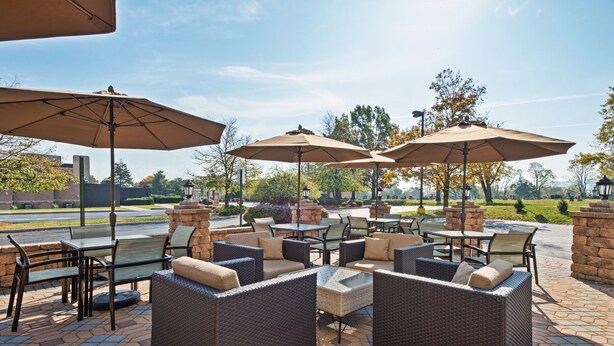 Une terrasse extérieure avec des meubles en osier, des piliers en pierre et de grands parasols.