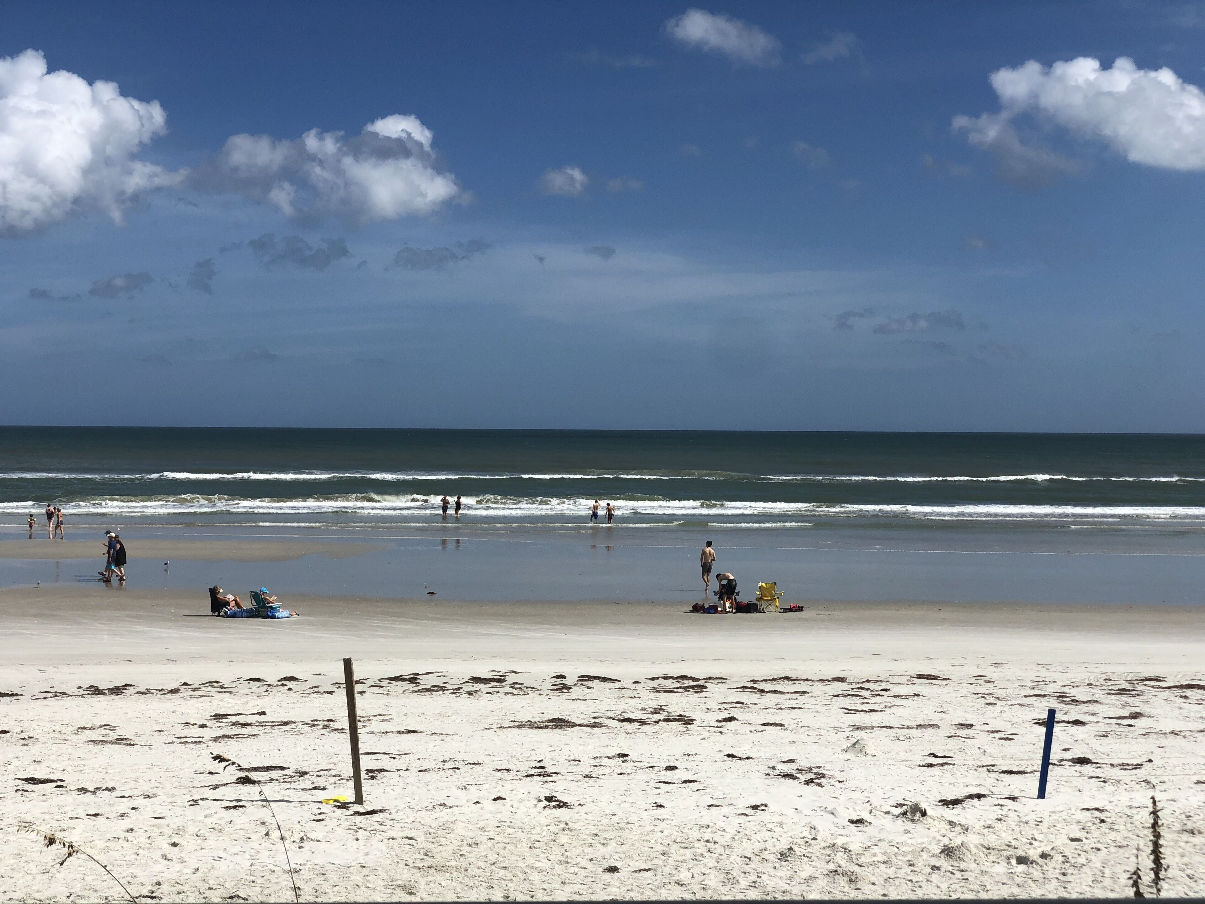 A beach with people walking and sitting on the sand, a clear sky, and the ocean in the background.