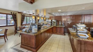 Un espace pour le petit-déjeuner à l’hôtel, avec un comptoir en marbre, un buffet proposant divers plats et des meubles de rangement en bois.