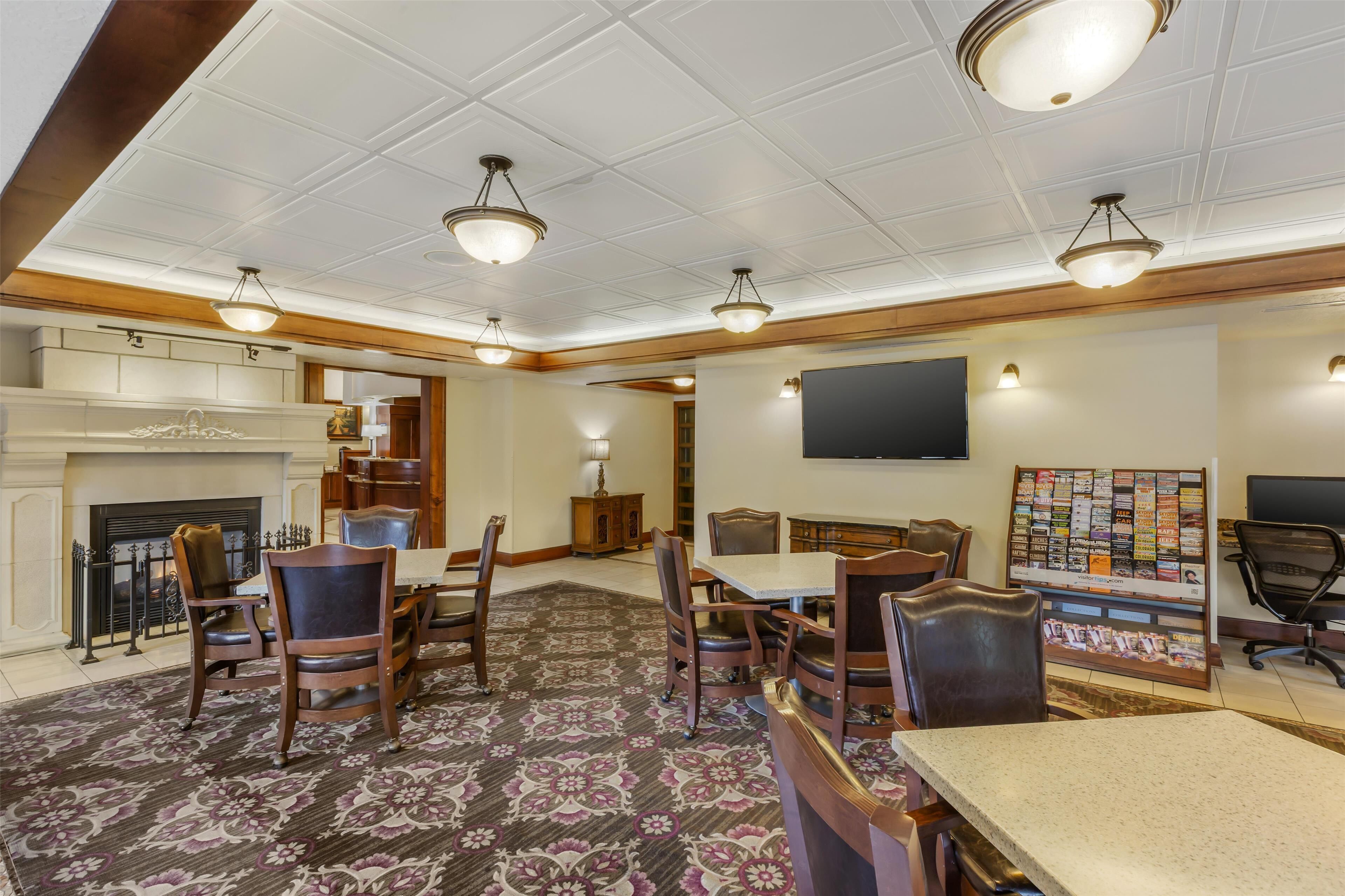 A spacious room with a fireplace, a television mounted on the wall, and a bulletin board displaying various items.