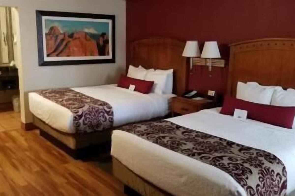 Quarto de hotel com duas camas, um quadro na parede e piso de madeira.