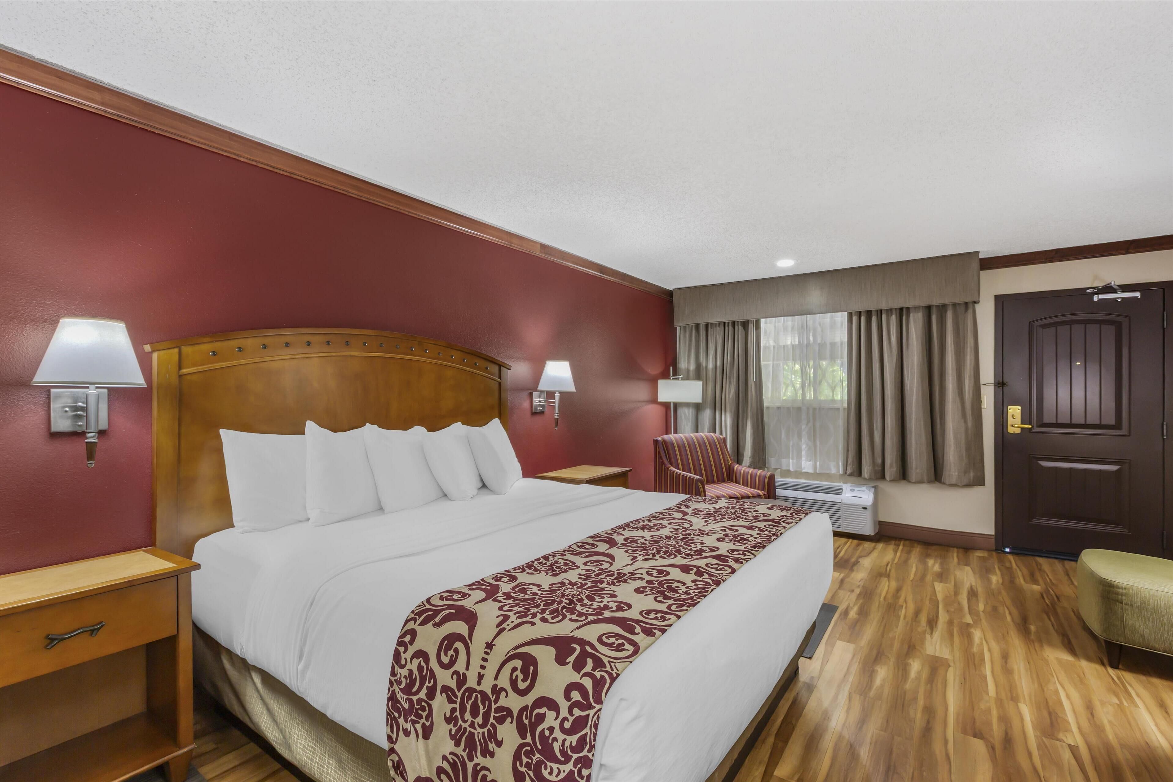 Una habitación de hotel con una cama grande, dos mesitas de noche, una silla, un escritorio y una ventana con cortinas.