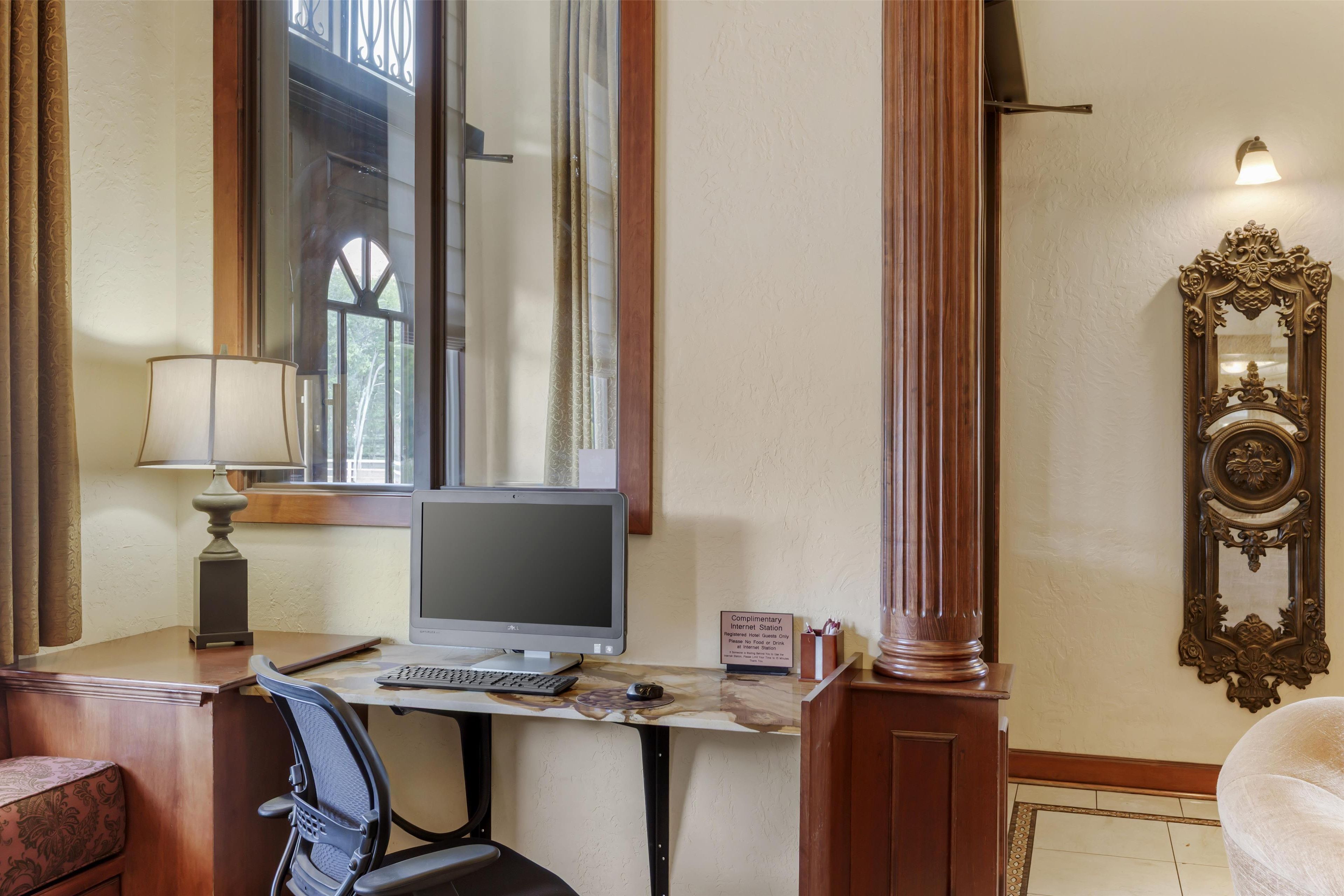 Une chambre d’hôtel équipée d’un bureau, d’un ordinateur, d’une chaise, d’une lampe et d’un grand miroir.