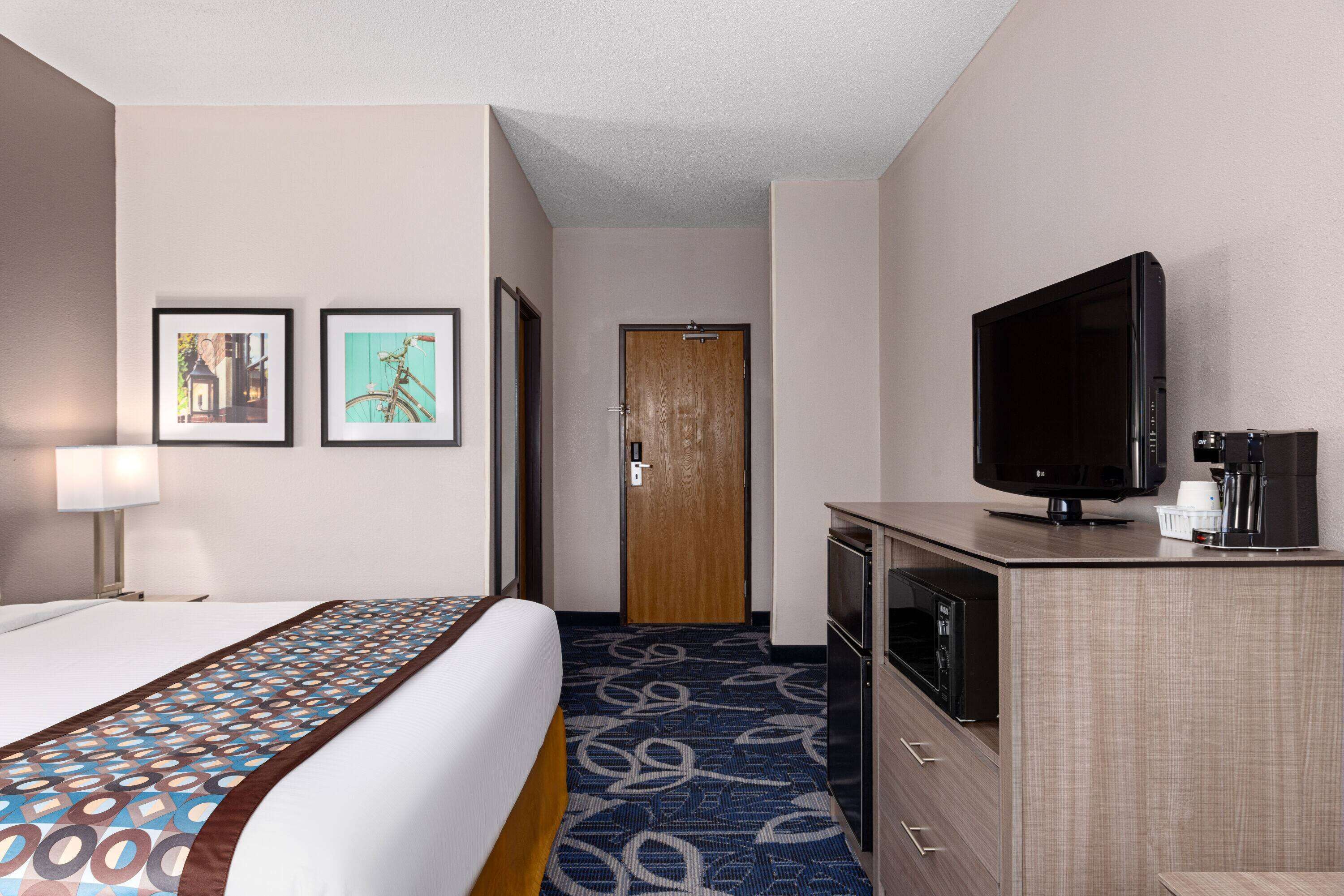 A hotel room with a bed, a television, a microwave, and a door leading to another room.