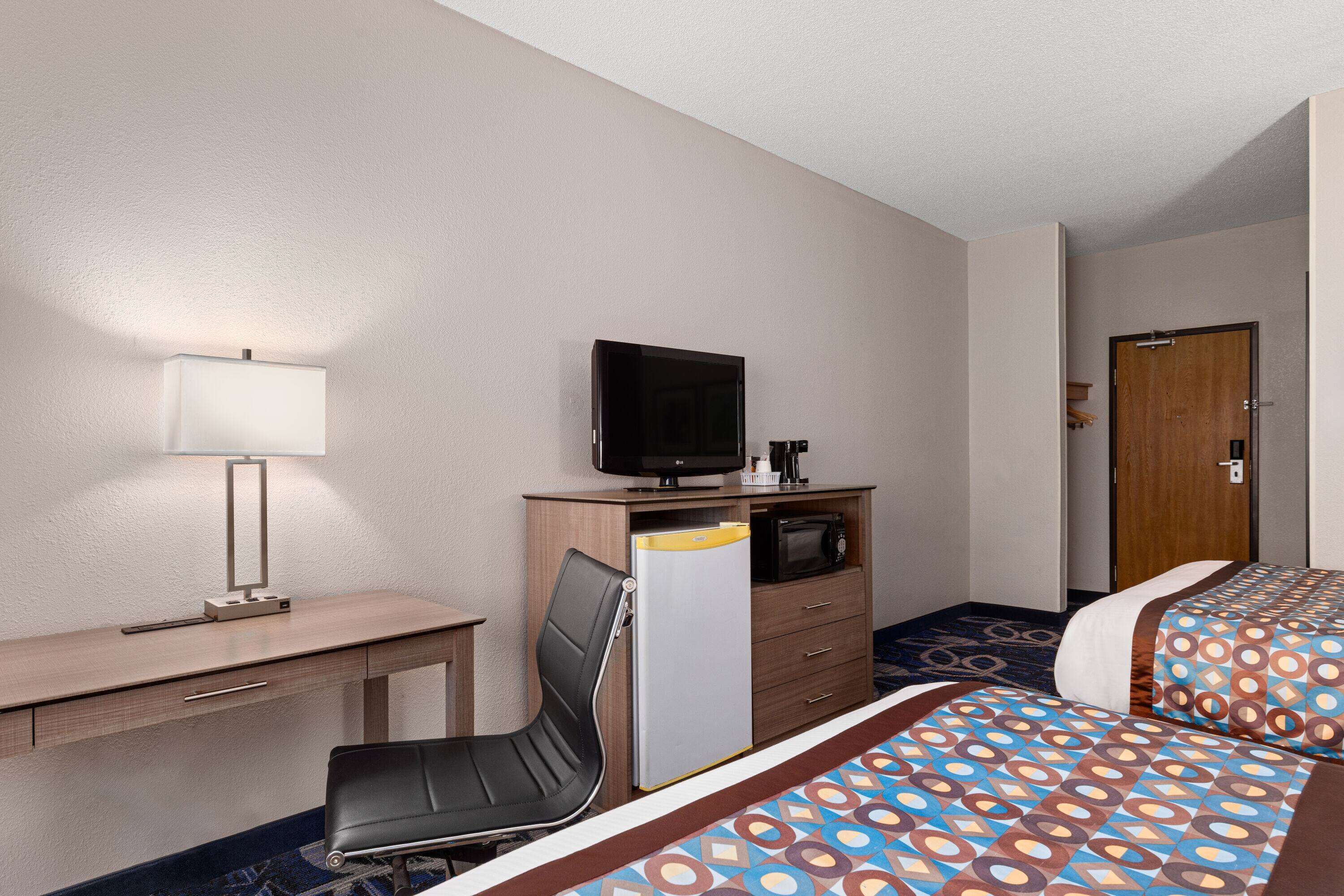Habitación de hotel con escritorio, silla, televisor, microondas, refrigerador y dos camas con ropa de cama estampada.