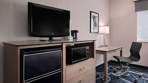 A hotel room with a flat-screen TV, a desk with a lamp, a chair, and a microwave.