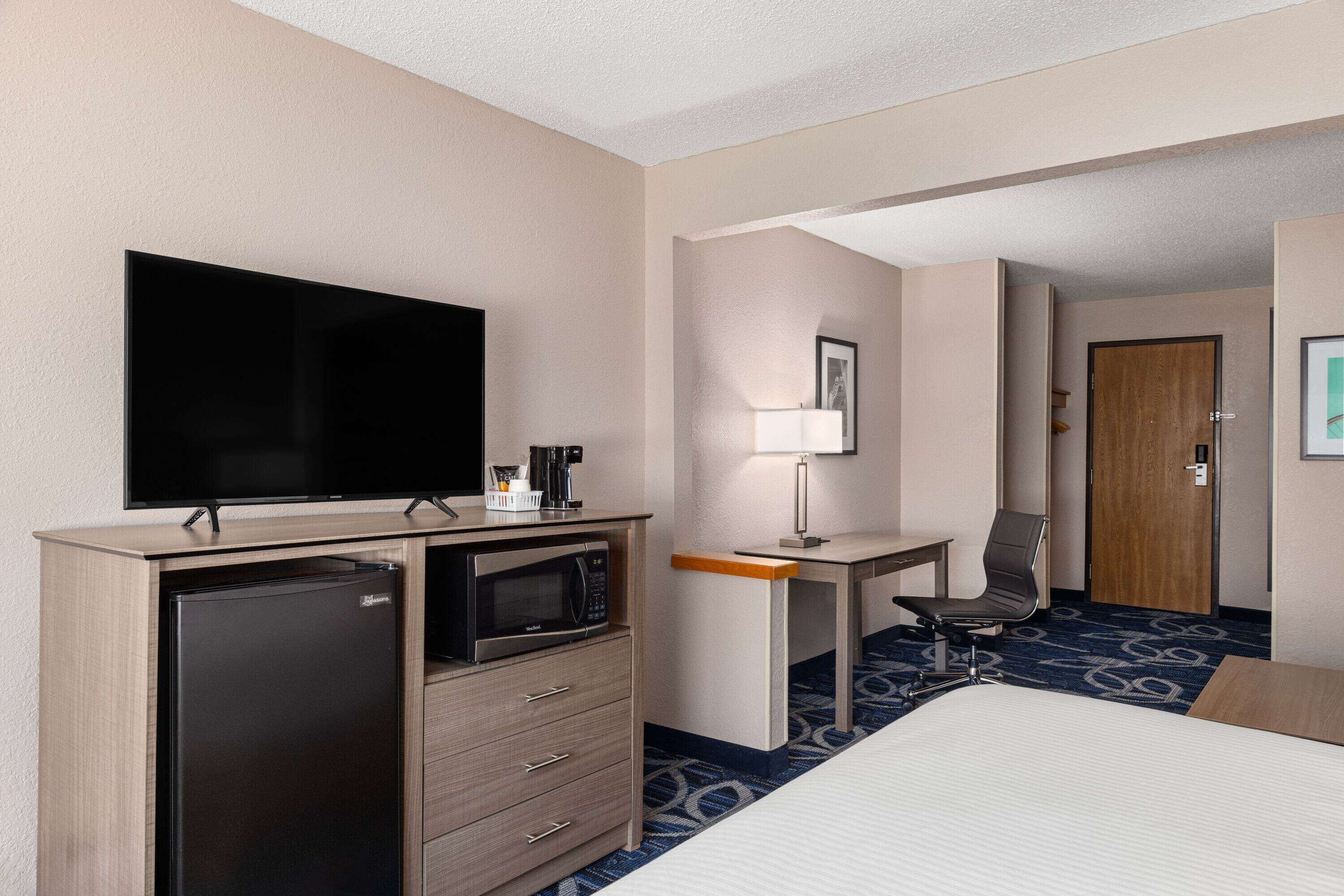 Una habitación de hotel con cama, escritorio con silla, televisión, refrigerador y microondas.