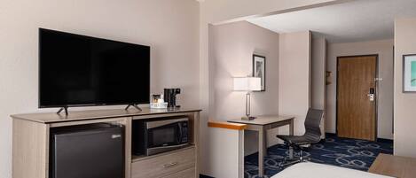 Una habitación de hotel con cama, escritorio con silla, televisión, refrigerador y microondas.