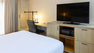 A hotel room with a bed, a desk with a chair, a flat-screen TV, a microwave, and a wardrobe.