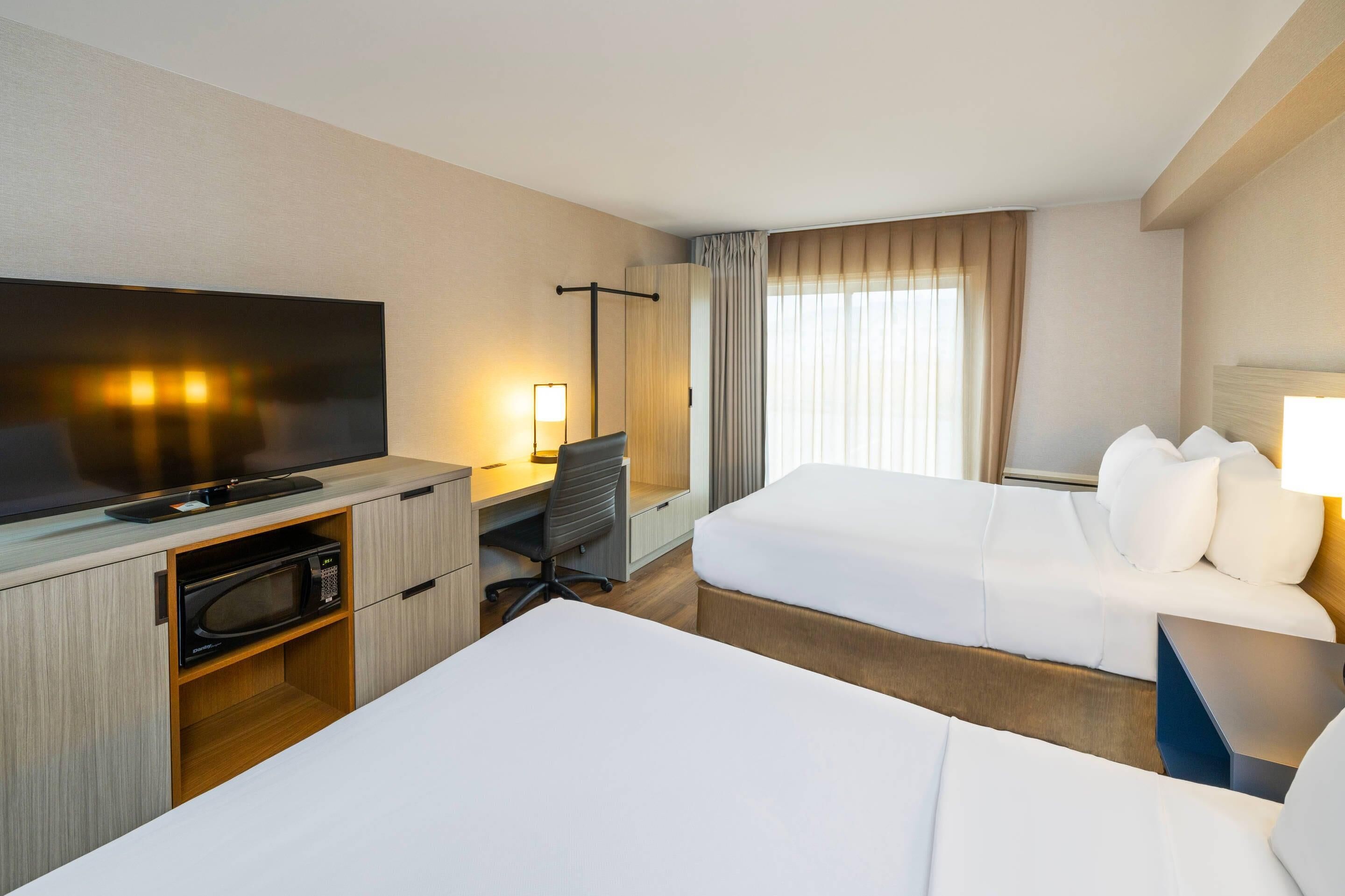 Una habitación de hotel con cama, escritorio, computadora, televisor y microondas.
