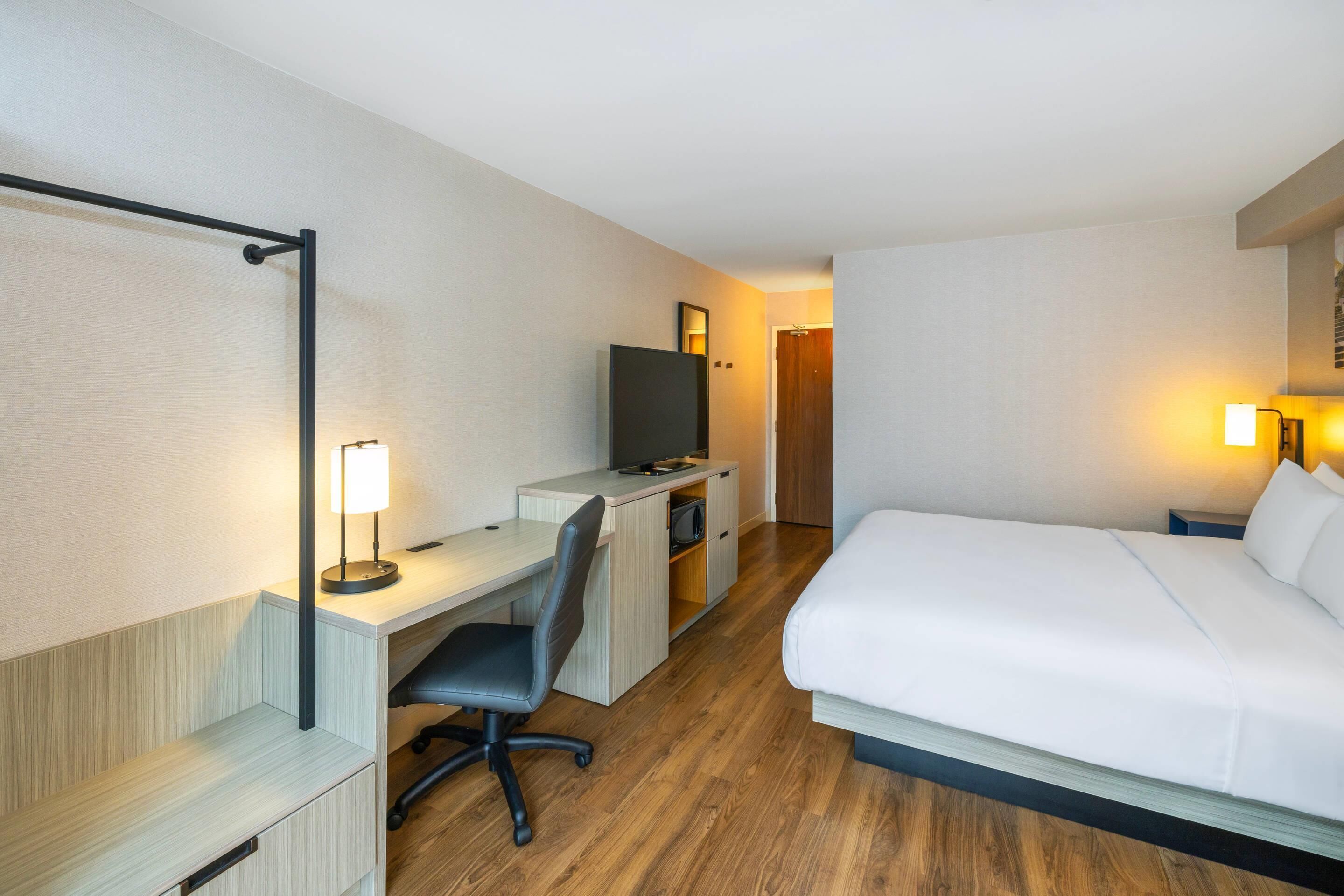 A hotel room with a bed, desk, chair, TV, and a door leading to another room.