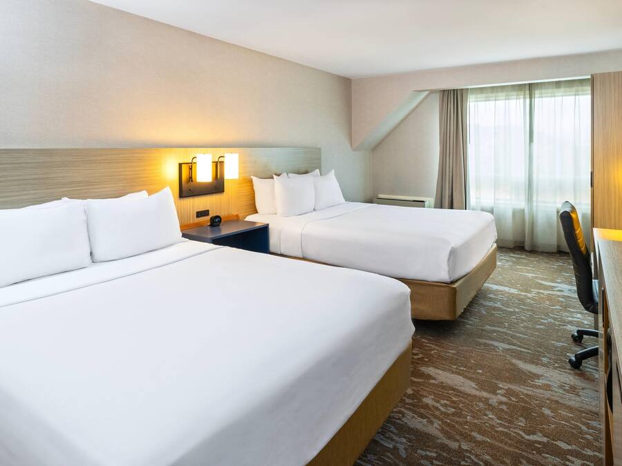 Een hotelkamer met twee bedden, een bureau, een stoel en een groot raam met gordijnen.